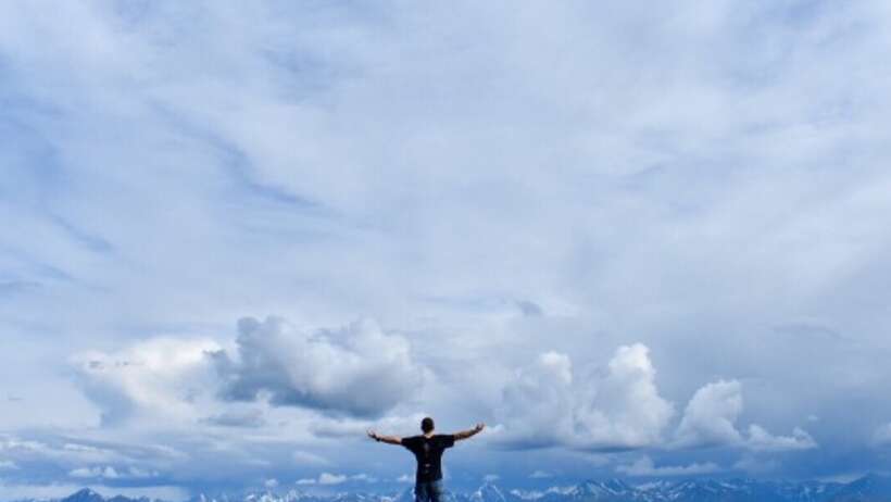Man on mountain top, arms outstretched, peaceful view.