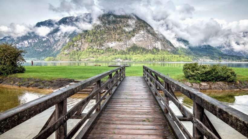 Lake with bridge, mountains and cloudy sky.