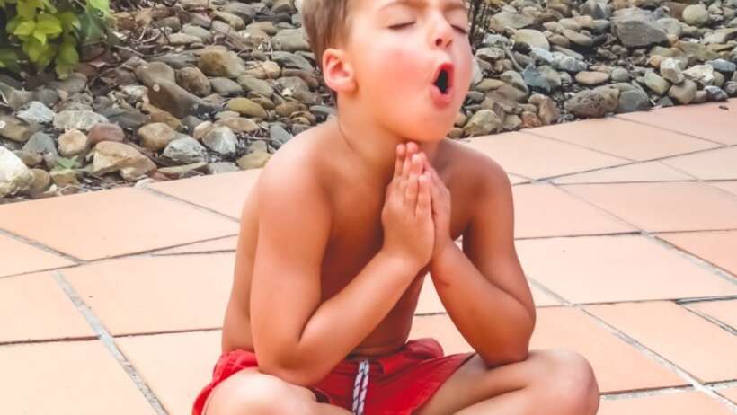 Boy meditating outdoors with hands in prayer position.